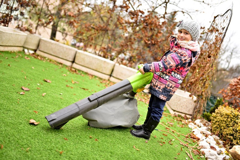 young girl with leaf blower in autumn